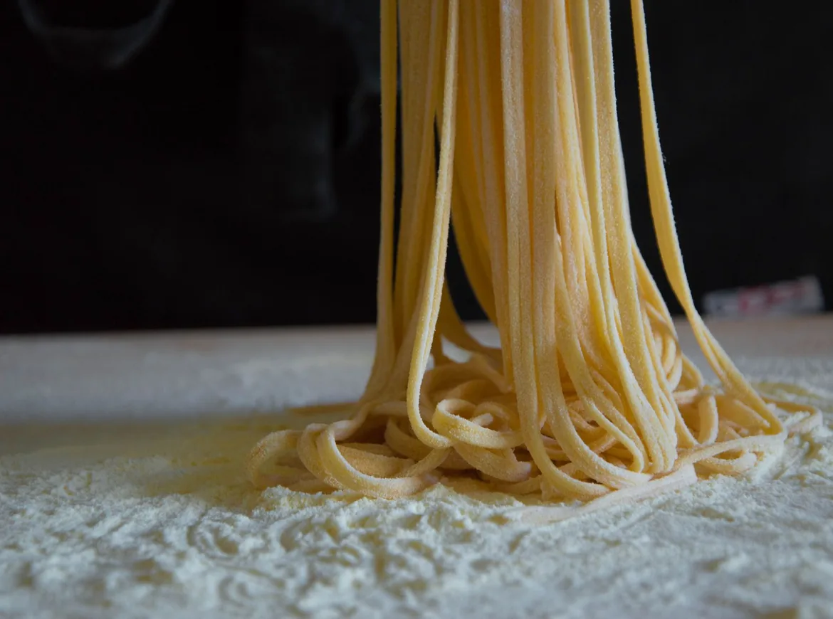 Stråler af frisk pasta stablet på et meldrysset bræt