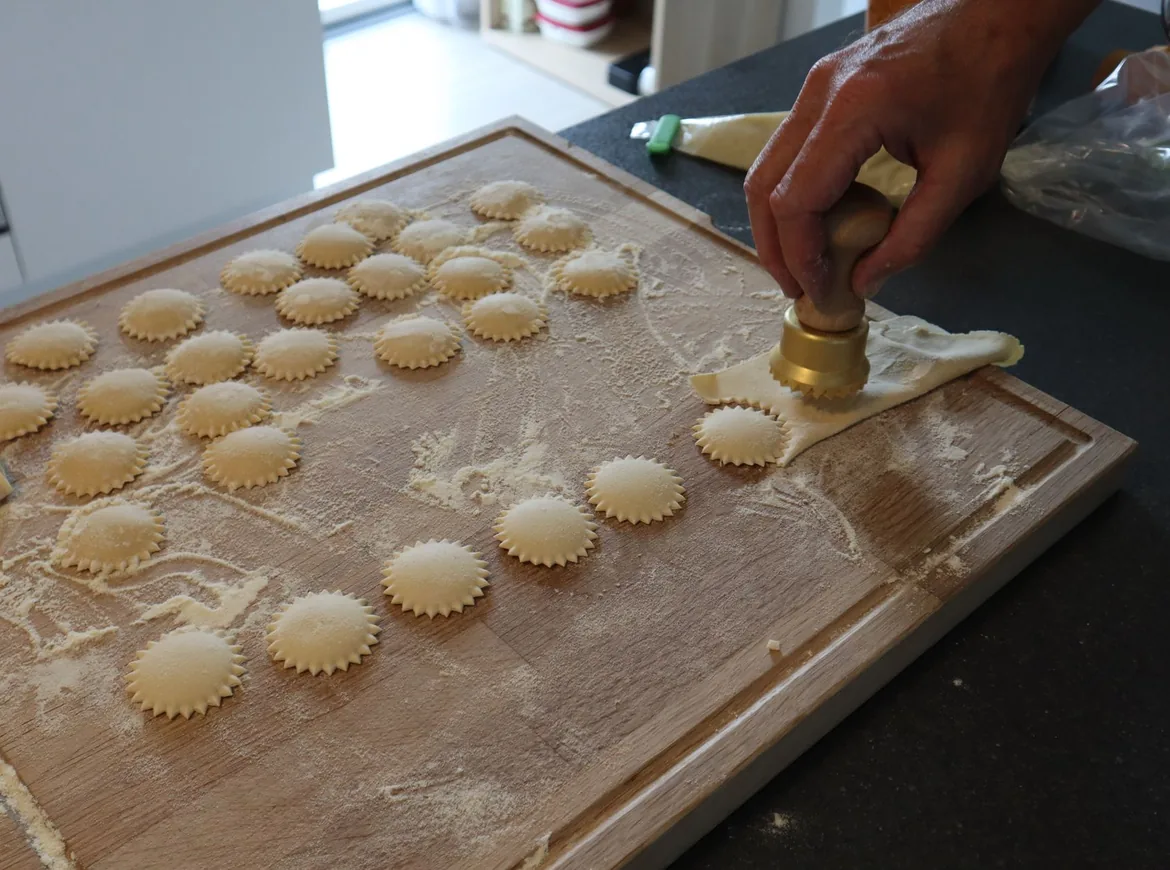 Rækker af bølgede ravioli på et melet træbræt ved siden af en udstikker