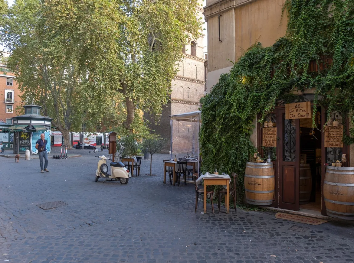 En stille romersk gade med en efeudækket trattoria, udendørsborde og en parkeret scooter